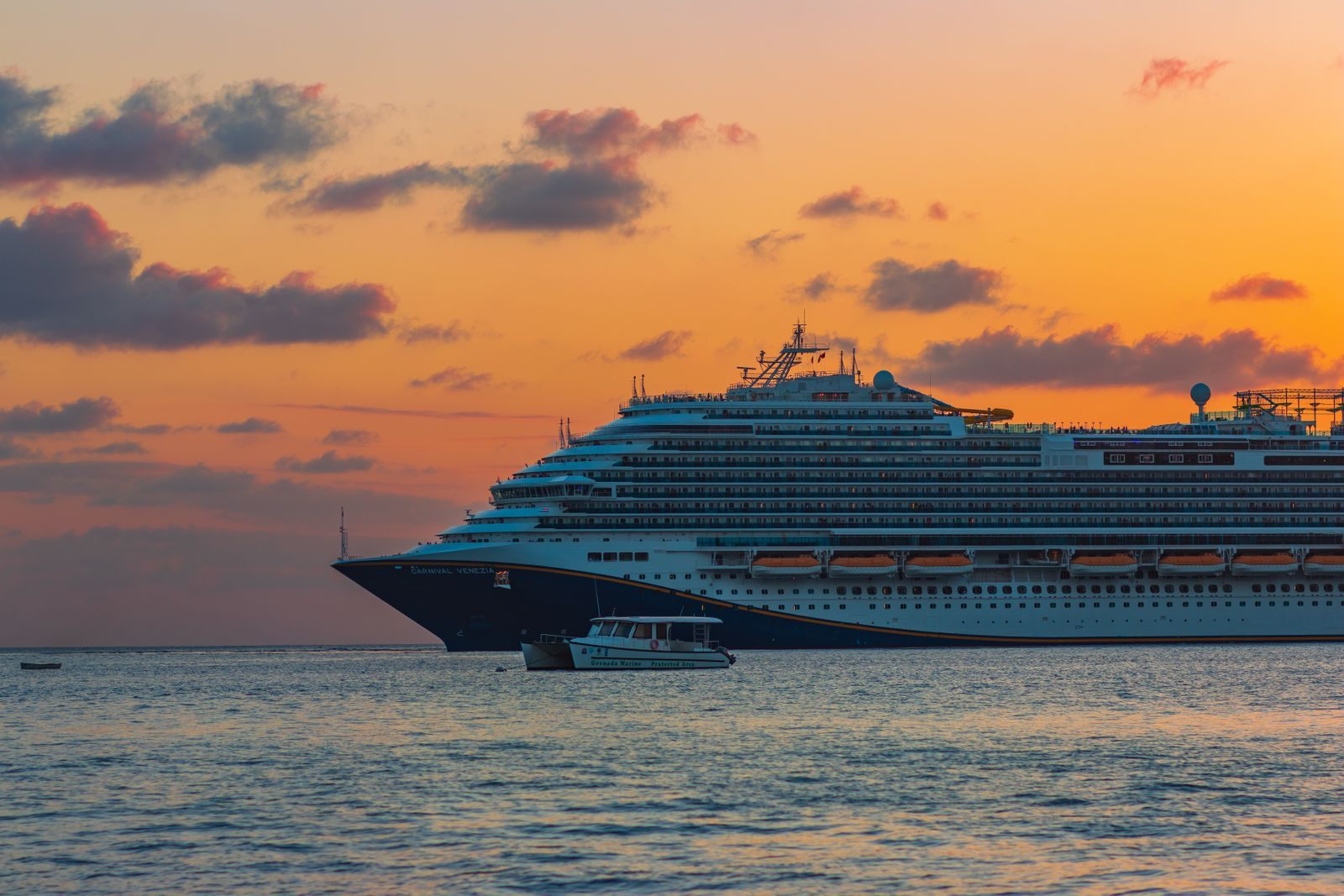 Large cruise ship sailing across calm sea under an orange sunset sky